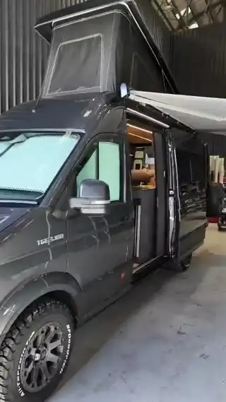 A finished grey pop-top campervan with its awning out, in the workshop