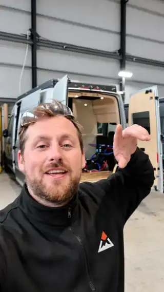 Ryan talking to camera in the workshop, in front of a van being converted